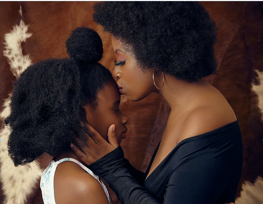 Une mère et sa fille portent deux afros volumineux. La maman embrasse le front de sa fille.